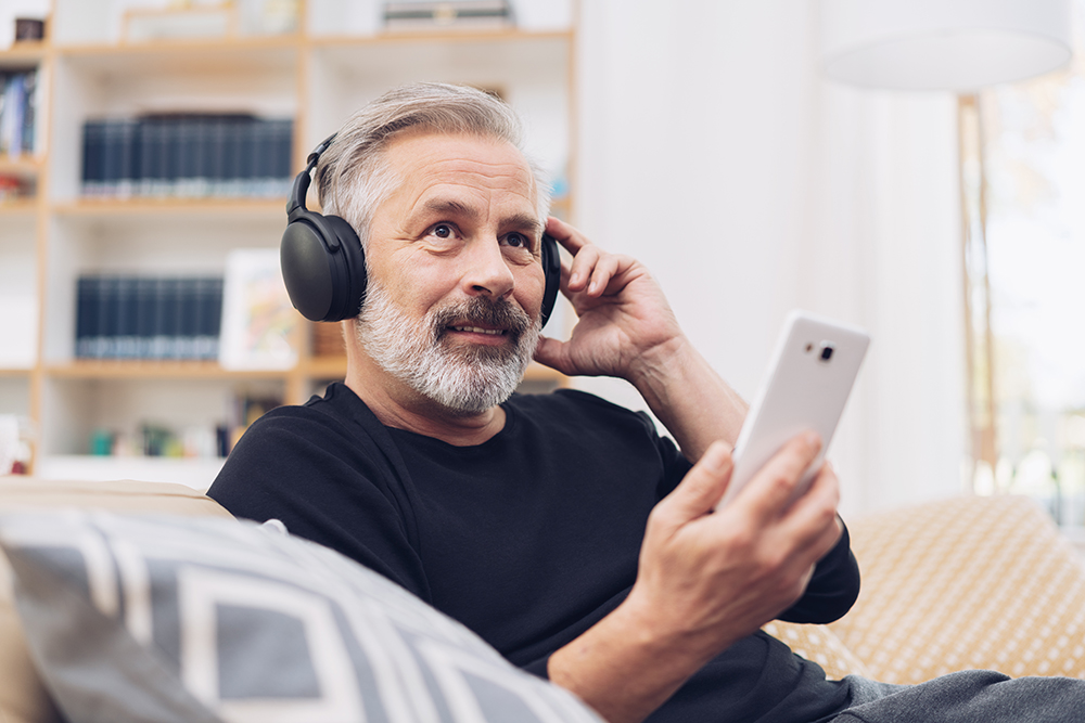 Portrait of a middle-aged man using his mobile phone for listening to Bob Russo's Realty Speak podcast: 1031 Like Kind Exchanges online through modern headphones at home