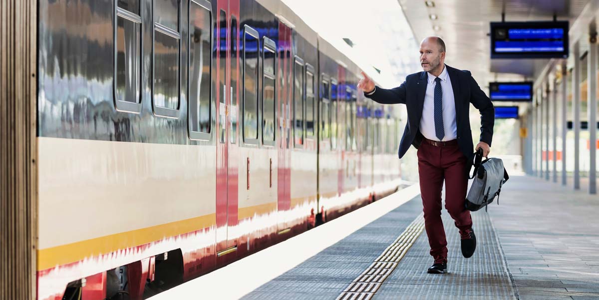 Image: A businessman holding a briefcase runs to catch up with and hop on a train as it departs a station.