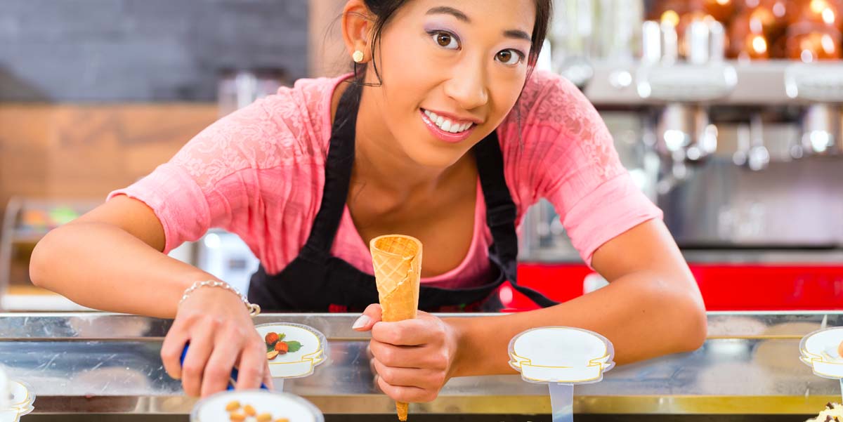 Asian American Teenage girl scooping ice cream with a smile in shop