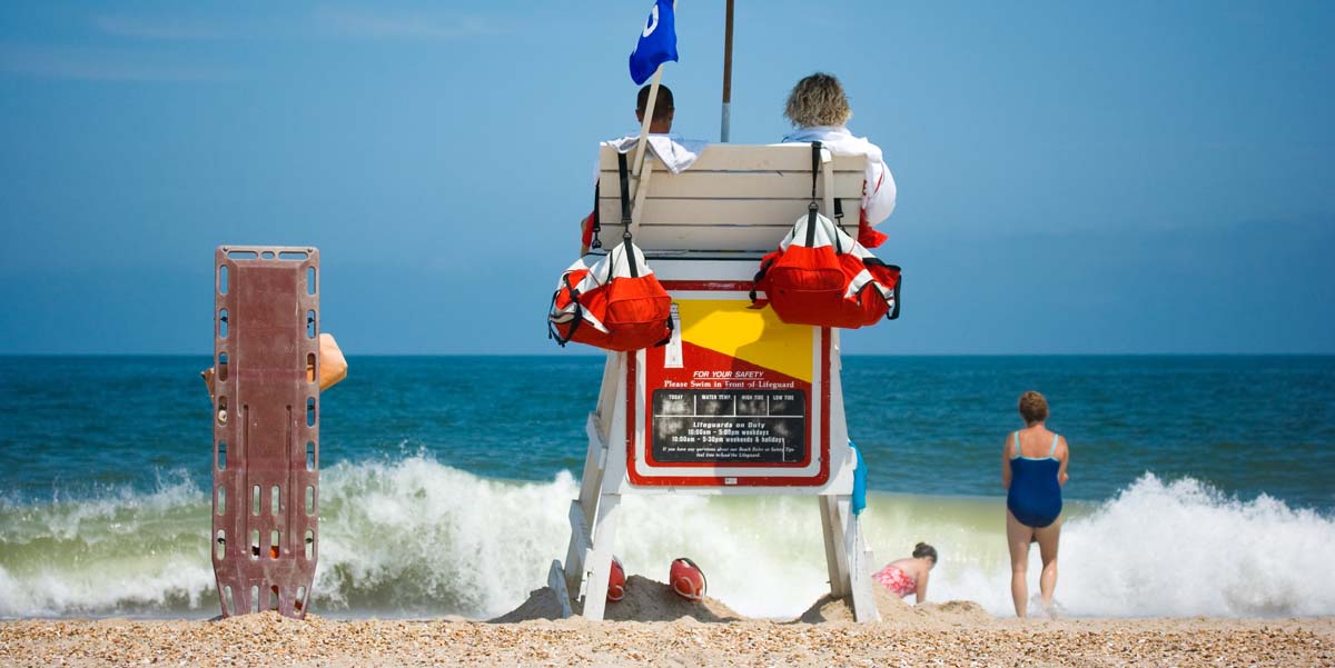 Two young male lifeguards watch ocean line while swimmers enjoy water on a sunny hot day