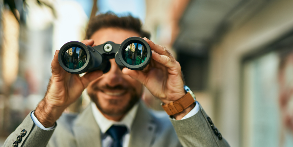 Russo CPA, What Are Estimated Tax Payments? A suited business man smiles as he looks through binoculars