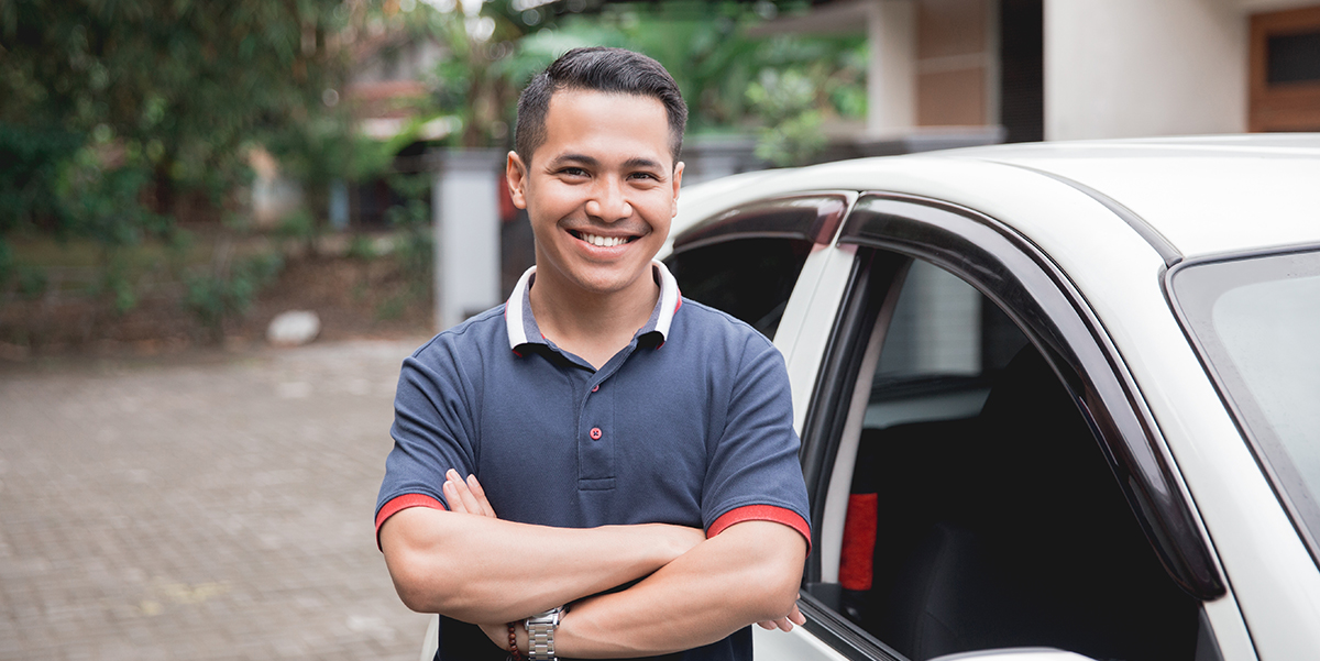 Smiling Asian man standing in front of his car with arms folded.