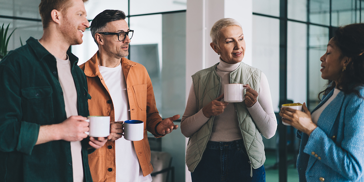 A group of men and women standing and discussing while drinking coffee.