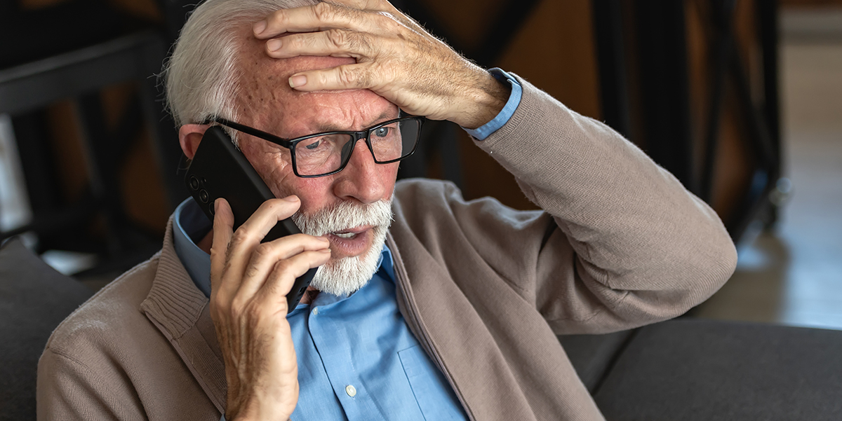 A retired man with hand on forehead on the phone looking worried.